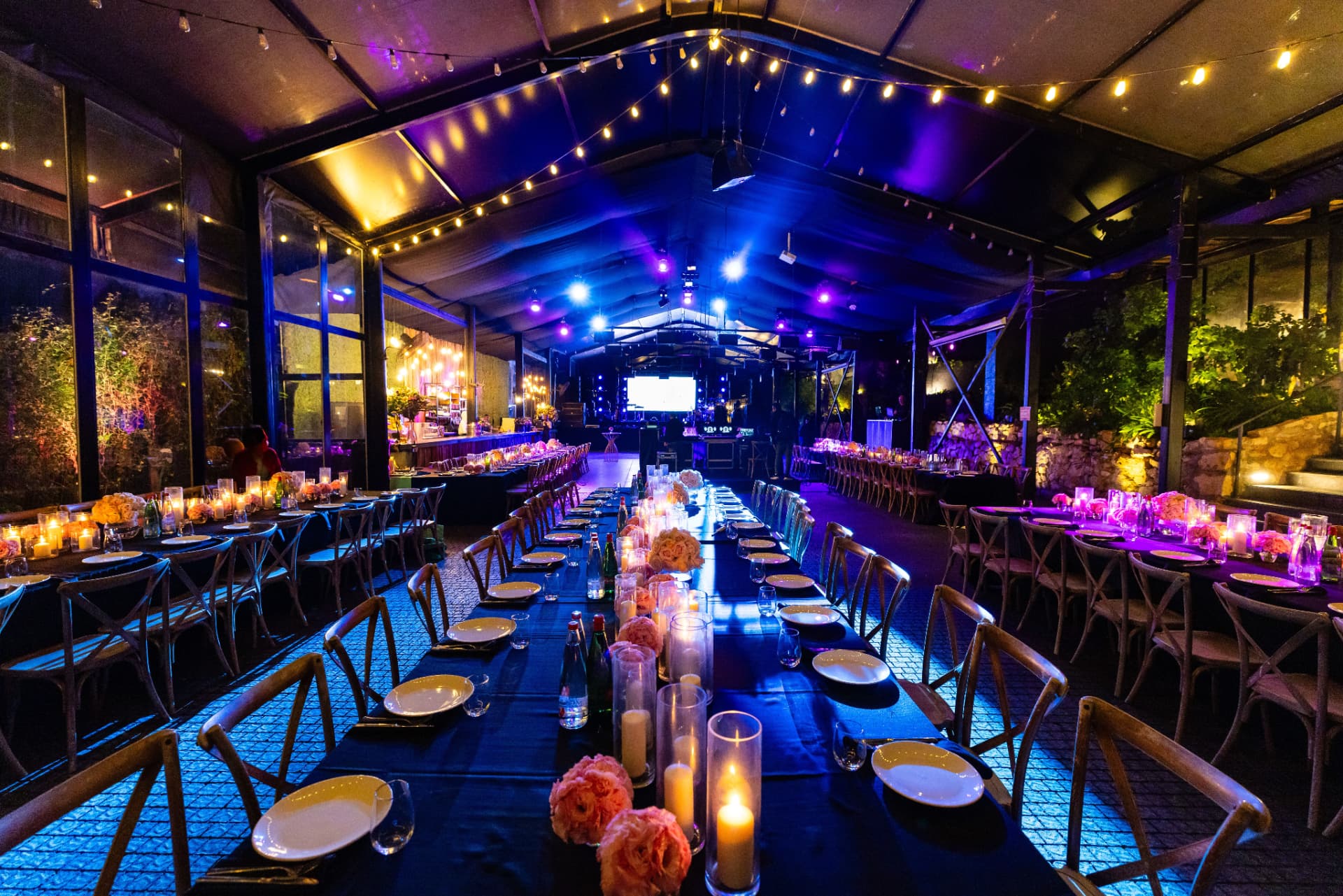 Fully produced gala venue by Memories in Motion — draped ceiling, lit stage, long banquet tables dressed with hire linens, glassware and centrepieces