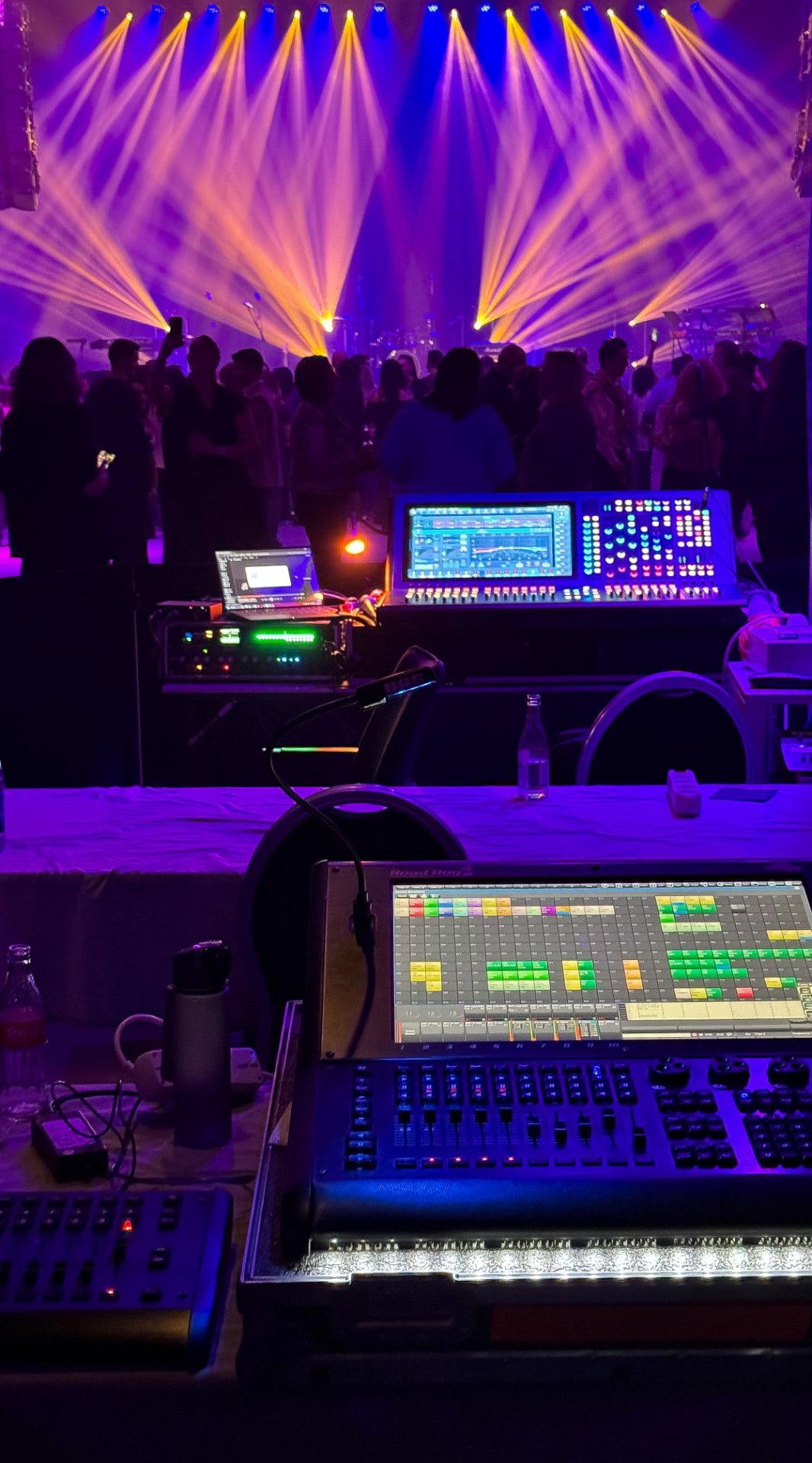 Front-of-house lighting and sound control desk run by Memories in Motion at a live hybrid event, with lit stage and audience beyond the console